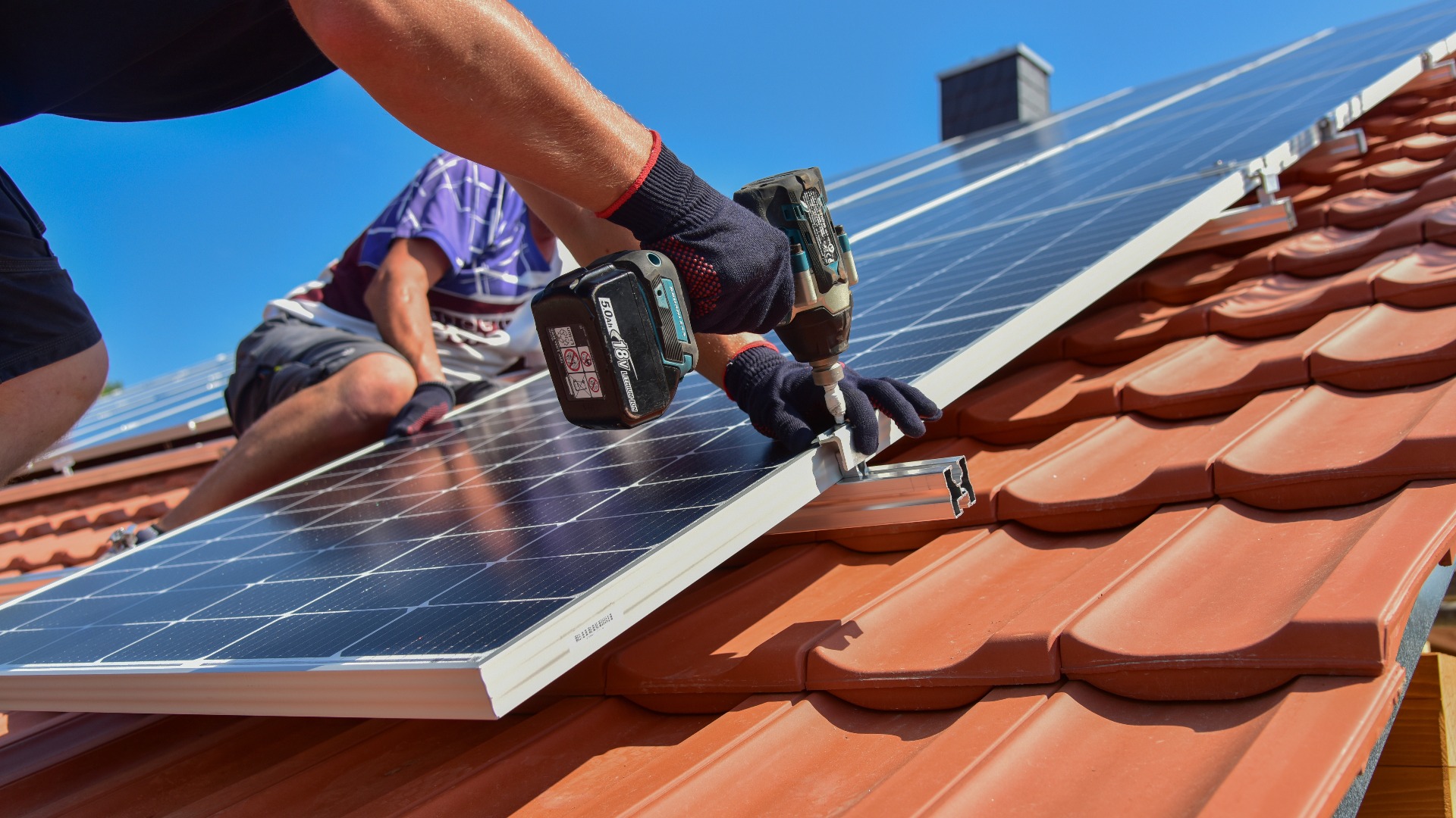 Dachdecker beim Aufbau einer Photovoltaikanlage auf einem neu gedeckten Ziegeldach: Verschraubung der Solarmodule an den Endklemmen des Schienensystems am Dachrand